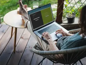 Frau sitzt mit Laptopf auf dem Schoß in einem Netzstuhl auf der Terasse und logt sich bei Dreamway-Travel ein.