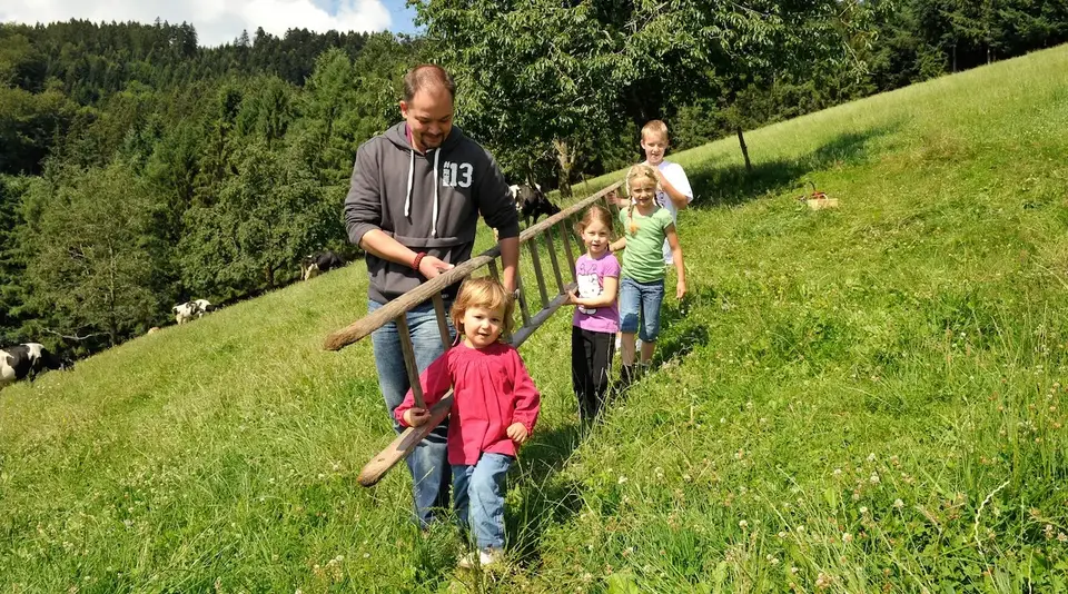 Wiesenabenteuer mit der Familie – Urlaub auf dem Land - © Susanne Mölle Eine Familie geht gemeinsam über eine grüne Wiese an einem Hang.