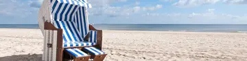 Weißer Strandkorb, Ostsee - © Superhasi, Adobe Stock Ein weiß-blau-gestreifter Strandkorb steht am Ostseestrand und lädt zum entspannten Landurlaub in Deutschland ein.