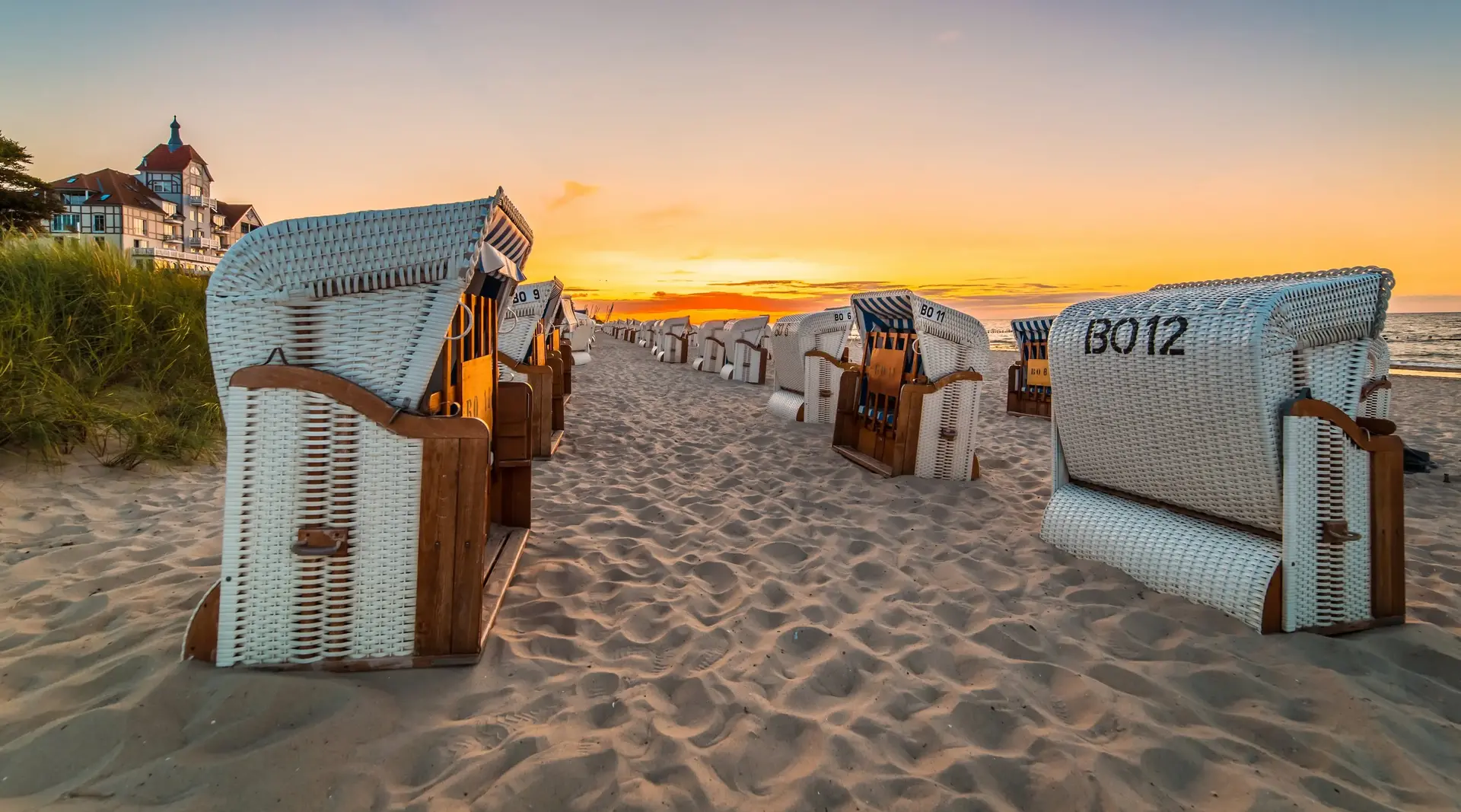 Sonnenuntergang an der Ostsee - © powell83, Adobe Stock mehrere Strandkörbe stehen bei Sonnenuntergang am Sandstrand an der Ostsee, der Himmel färbt sich orange