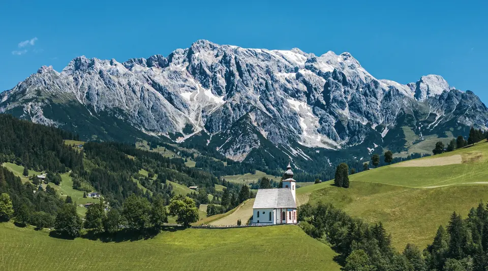 Eine kleine Kapelle steht auf einem Grünem Hügel vor großem Felsmassiv dem Hochkönig im Pinzgau im Bundesland Salzburg in Österreich