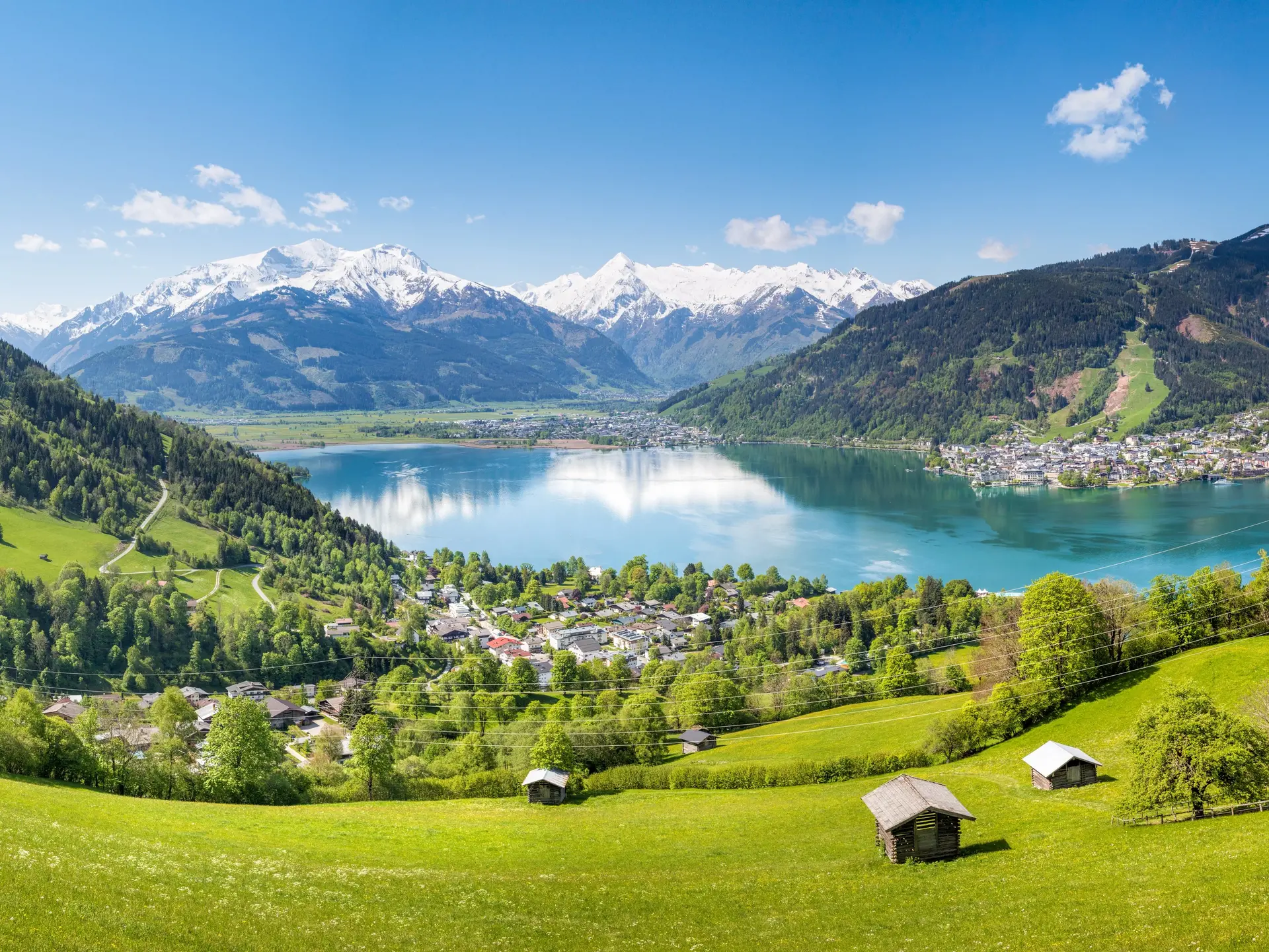 Blick auf einen blauen See im Sommer mit weißen Schneebergen im Hintergrund.