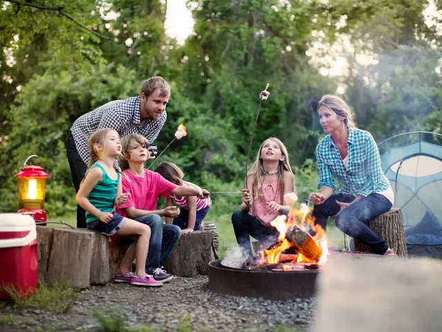 Eltern mit Kindern sitzen am Lagerfeuer vor ihrem Zelt und rösten Marshmallows