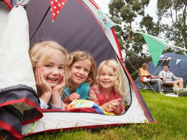 Kleine Entdecker, großes Abenteuer – Familiencamping auf dem Bauernhof - © micromonkey, adobe stock Blick aus dem Zelt: Drei Kinder beobachten neugierig das Geschehen draußen, wo ihre Eltern im Hintergrund den Moment genießen – Familienzeit pur beim Camping auf dem Bauernhof.