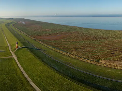 Pilsumer Leuchtturm in Ostfriesland - © Christian, Adobe Stock alt="Blick von oben auf den Nordseedeich mit dem Pilsumer Leuchtturm, Ostfriesland"