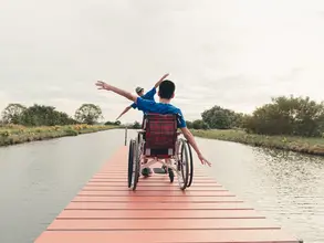 Barrierefreier Urlaub auf dem Land – gemeinsame Auszeit am See - © AdobeStock - GAYSORN Mann im Rollstuhl sitzt mit seinem Vater auf einem Holzsteg an einem See während eines barrierefreien Urlaubs auf dem Land