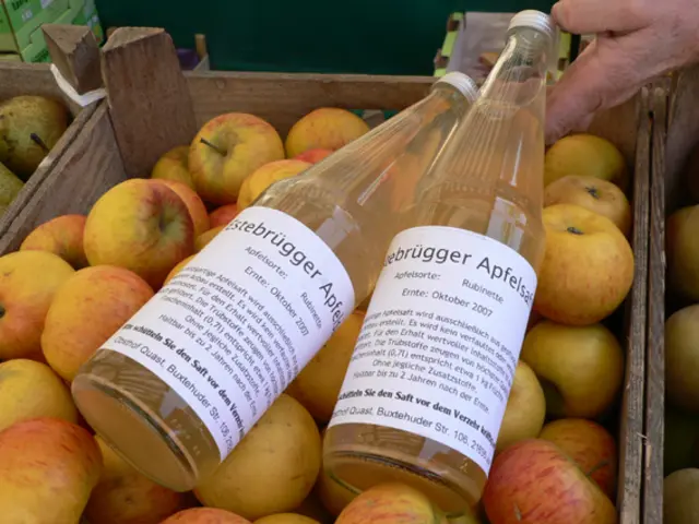 zwei Glasflaschen mit Apfelsaft auf einer Kiste mit frischen Äpfeln