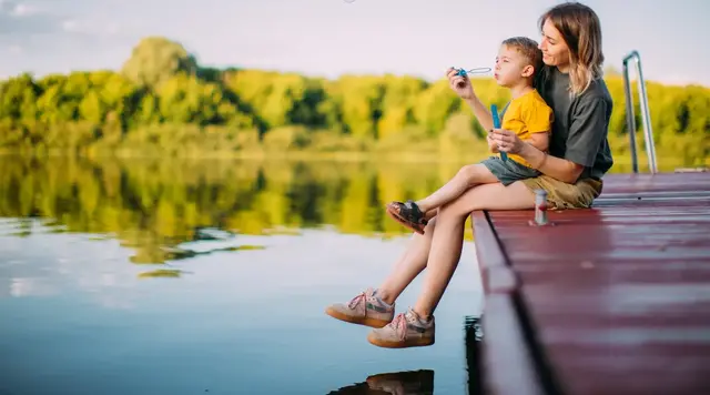 Unbeschwerte Familienzeit am Ferienhaus in der Natur Mutter und kleiner Junge sitzen auf einem Holzsteg in ländlicher Natur und lassen Seifenblasen steigen – idyllische Szene im Sommerurlaub beim Ferienhaus auf dem Land.