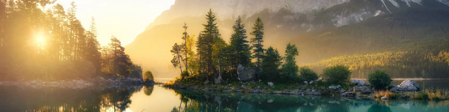 Idyllischer See bei Sonnenaufgang, ein malerisches Panorama mit majestätischen Bergen und dem goldenen Sonnenlicht, das hinter den Bäumen hereinscheint