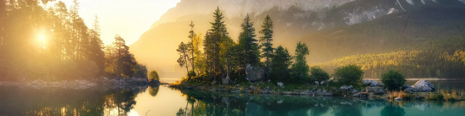 Idyllischer See bei Sonnenaufgang, ein malerisches Panorama mit majestätischen Bergen und dem goldenen Sonnenlicht, das hinter den Bäumen hereinscheint