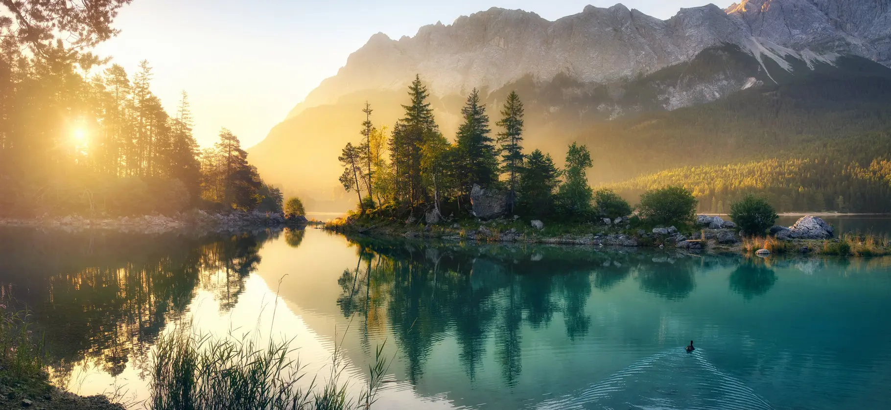 Idyllischer See bei Sonnenaufgang, ein malerisches Panorama mit majestätischen Bergen und dem goldenen Sonnenlicht, das hinter den Bäumen hereinscheint