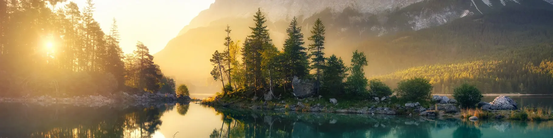 Idyllischer See bei Sonnenaufgang, ein malerisches Panorama mit majestätischen Bergen und dem goldenen Sonnenlicht, das hinter den Bäumen hereinscheint