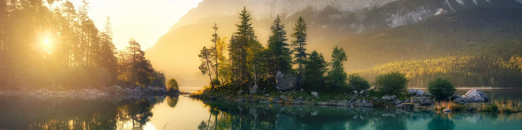 Idyllischer See bei Sonnenaufgang, ein malerisches Panorama mit majestätischen Bergen und dem goldenen Sonnenlicht, das hinter den Bäumen hereinscheint