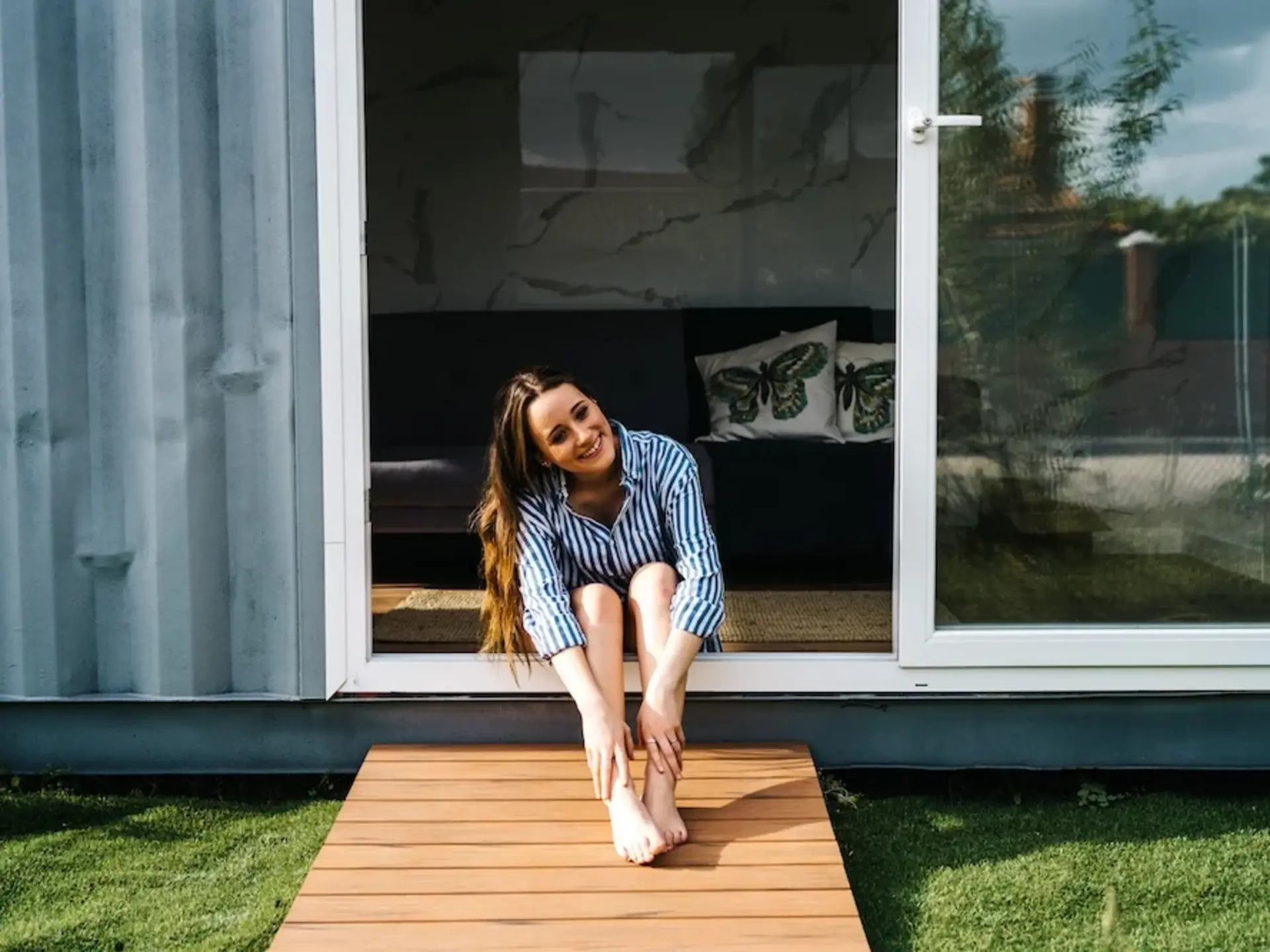 Tiny House - Außergewöhnliche Ferienhäuser auf dem Land - © Jake Jakab, adobe stock Frau sitzt an geöffneter Glastüre eines Tiny Houses