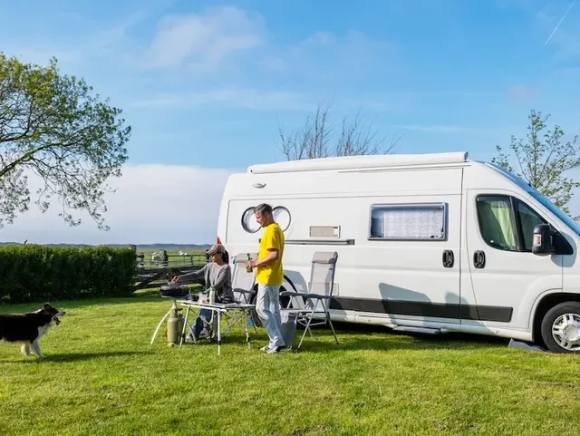 Naturgenuss pur – Mit Hund und Campervan beim Bauernhofurlaub - © Fokke Baarssen, adobe stock Zwei Menschen und ihr Hund genießen die Natur vor ihrem weißen Camper-Kastenwagen – Campingidylle auf der Wiese.