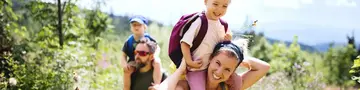 - © Halfpoint – stock.adobe.com  Vorderansicht einer Familie mit kleinen Kindern beim Wandern im Freien in der sommerlichen Natur.