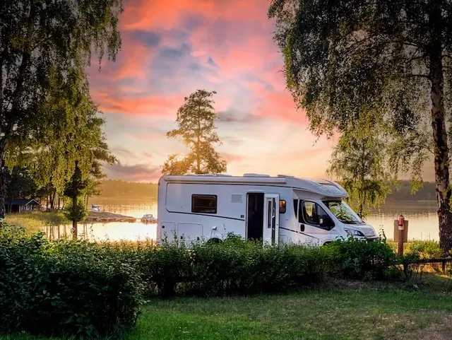 Bauernhof-Romantik: Mit dem Campervan ins Naturabenteuer - © NIKIBA, adobe stock Ein weißer Campervan steht am Ufer eines Sees, der Himmel leuchtet rosa in der Abenddämmerung – stimmungsvolle Szene beim Urlaub auf dem Bauernhof.