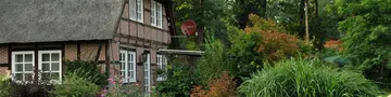 Urlaub im Landhotel und Landgasthof Fachwerkhaus mit Krüppelwalmdach ist mit Schilf gedeckt und umgeben von grünen Büschen